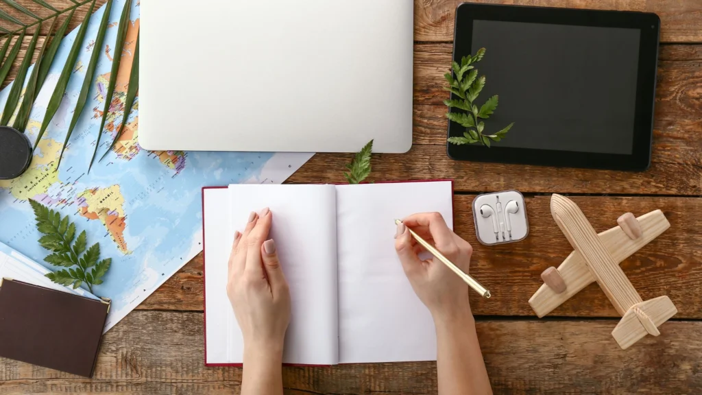 Overhead view of a travel planning workspace with a notebook, map, and travel-themed items