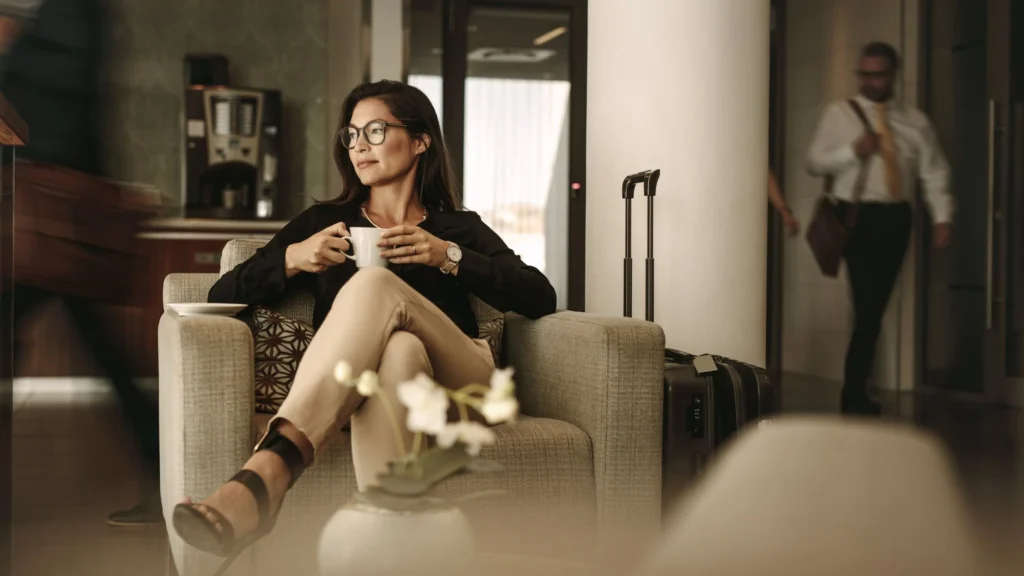 A woman enjoying a cup of coffee in an upscale airport lounge with a suitcase beside her
