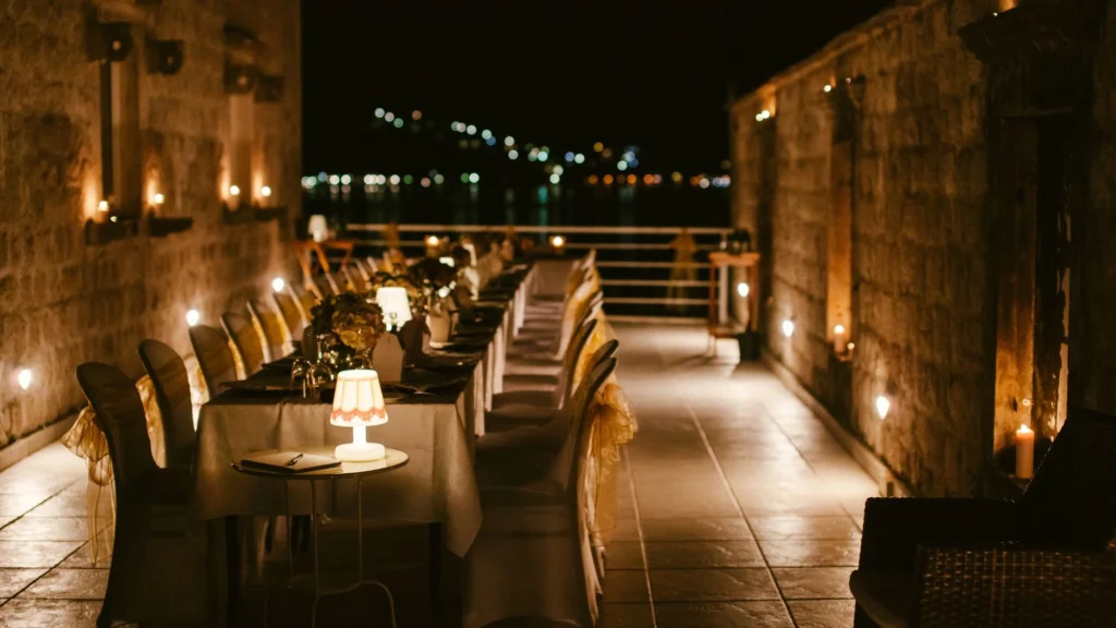  An elegant outdoor dining setup with string lights and candles overlooking the night skyline