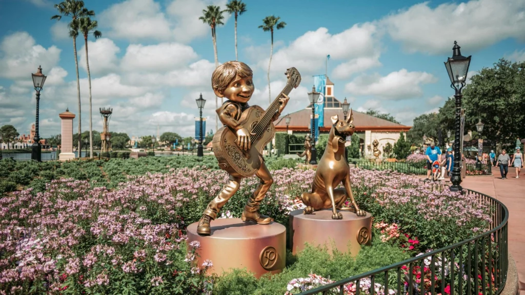 A golden Coco statue at EPCOT surrounded by vibrant flowers and a lively atmosphere