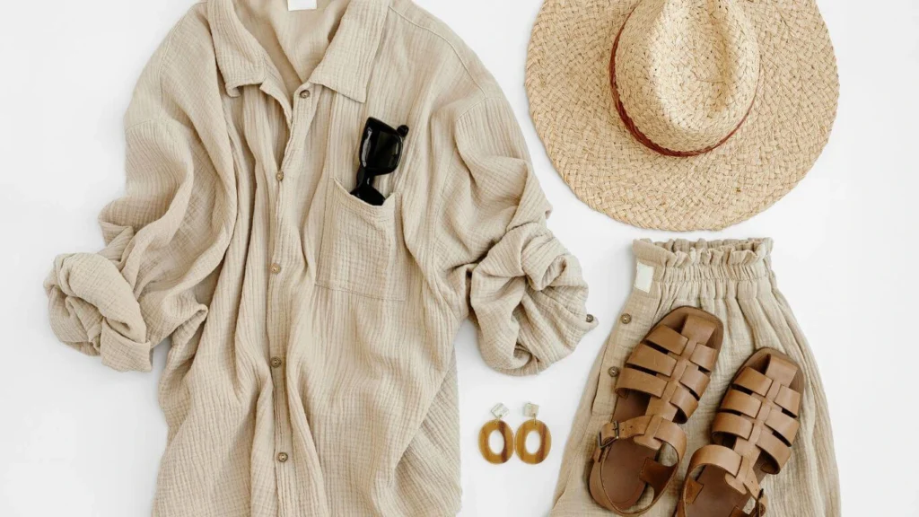 Flat lay of women's summer fashion: linen shirt, straw hat, sandals, and skirt.