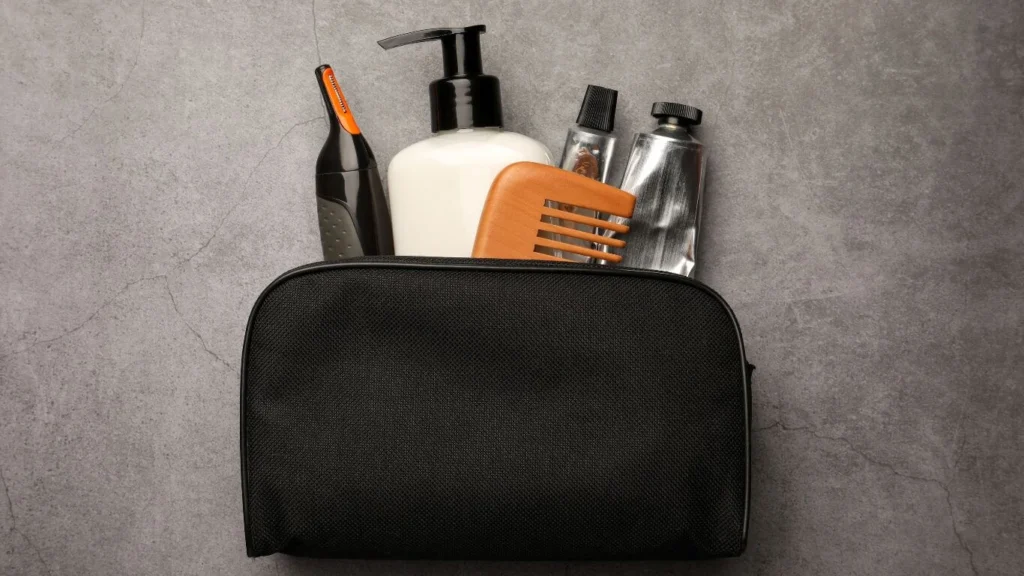 Open black toiletry bag with men's grooming products on a gray background.